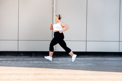 Full length of woman jogging against wall