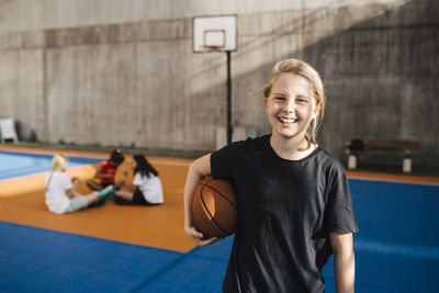 Portrait of smiling girl with basketball at sports court