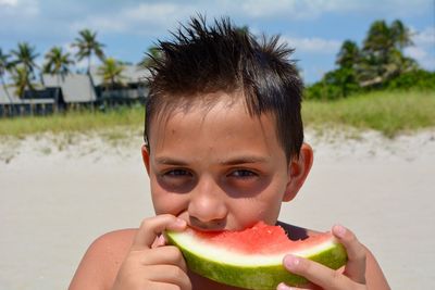 Portrait of boy eating watermelon at beach during sunny day