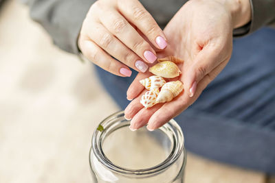 Women's hands hold seashells. puts the shells in a glass jar. beach treasures.
