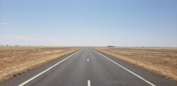 Road amidst field against clear sky