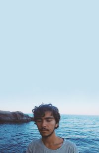 Man with eyes closed resting on sea against clear sky