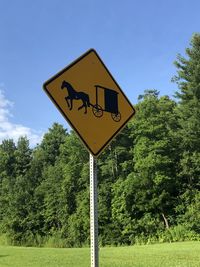 Road sign by trees on field against sky