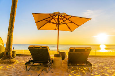 Deck chairs on beach against sky during sunset