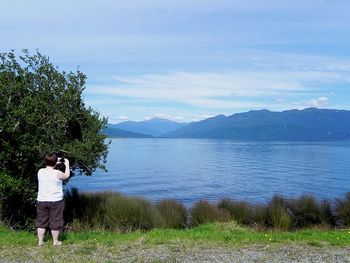 Woman photographing lake by trees