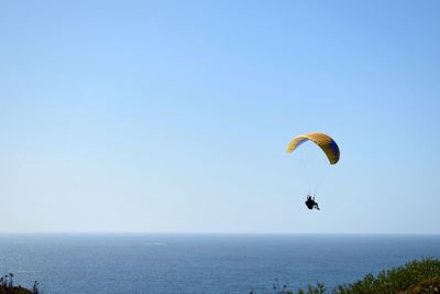 Man paragliding over sea against clear sky