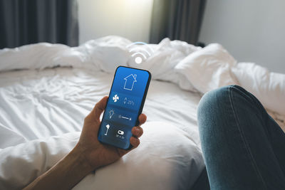 Low section of person using mobile phone on bed at home