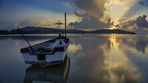 Empty fishing boat moored at lake during sunset