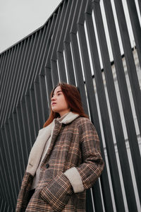 Young woman looking away while standing by wall