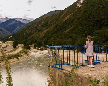 Rear view of woman standing by railing against mountains