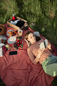 Young woman reading book on picnic blanket in field