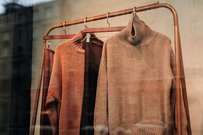 Brown beige knitted sweaters hanging in a row on a hanger in the window of a women's fashion store