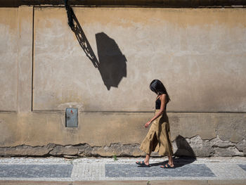 Side view of woman walking on sidewalk against wall
