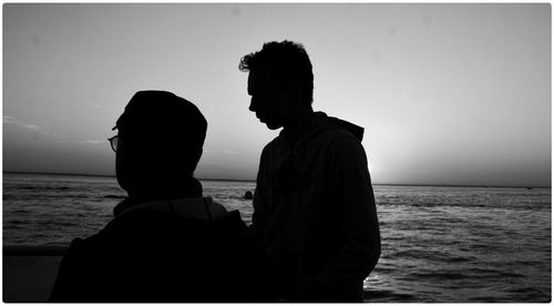 Silhouette men standing at beach against clear sky