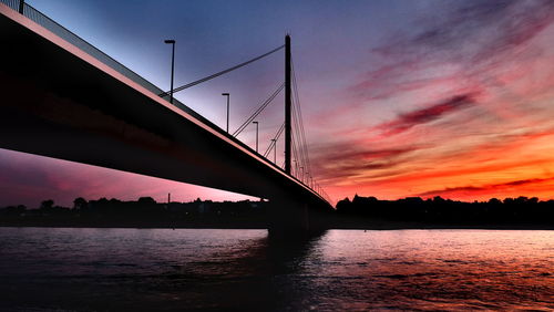 Silhouette bridge over river against sky at sunset