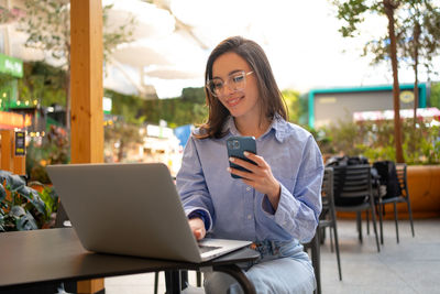 Young woman using mobile phone while sitting at cafe