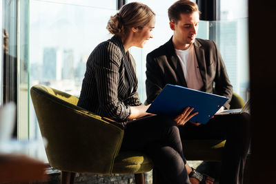 Colleagues discussing over laptop while sitting in office