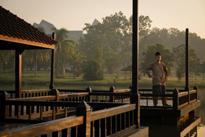 Man standing on table by railing against trees