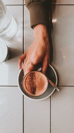 Cropped hand of woman holding coffee cup on floor