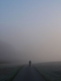 Rear view of man riding bicycle on road during foggy weather