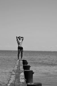 Full length of young woman standing at beach against clear sky