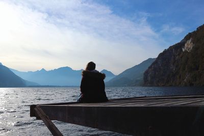 Woman sitting by sea against sky