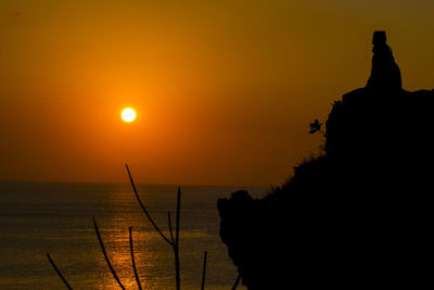 Silhouette rocks by sea against sky during sunset