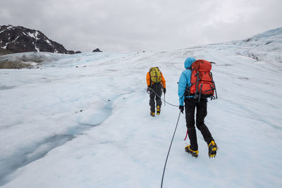 Rear view of people hiking on snow covered mountains against cloudy sky