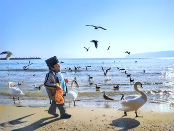 Dwarf man with birds at beach against clear blue sky