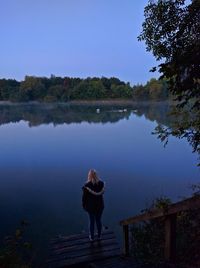 Rear view of man standing by lake against clear sky