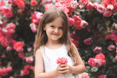 Cute baby girl 5-6 year old hold rose flower sit over bloom bushes in garden outdoor. spring season