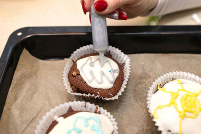 A woman squeezes colored frosting from a tube onto chocolate brown cupcakes covered white frosting.