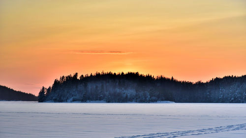 Scenic view of snow covered landscape against orange sky