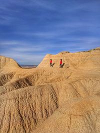 People walking on rock formation against blue sky