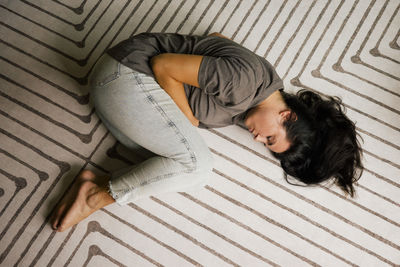 Directly above of lonely woman lying down in fetal position on carpet at home