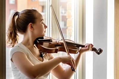 Young woman playing violin by window