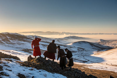 Rear view of people on snow covered land during sunset