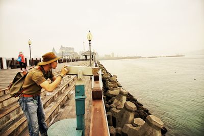 Side view of man using coin operated binoculars by river