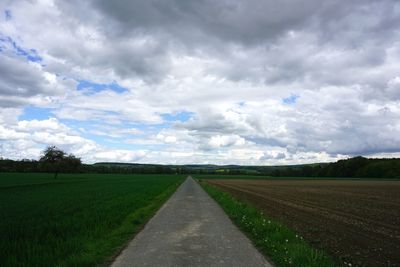 Empty road amidst agricultural field against sky