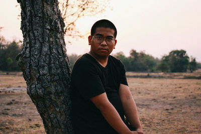 Portrait of young man standing on tree trunk