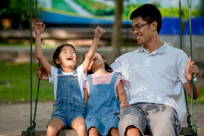 Happy father sitting with cheerful daughters on swing at park