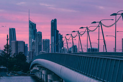 Bridge over city buildings against sky during sunset