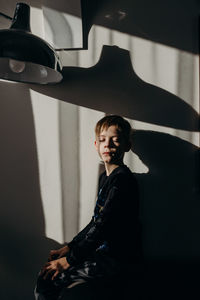 Side view of boy with eyes closed sitting by wall