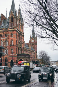 Black cabs driving along asphalt road outside medieval brick building on gray rainy day in city