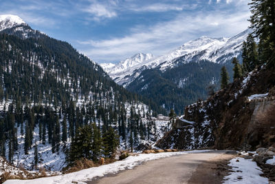 Road by snowcapped mountains against sky during winter