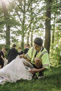 Full length of boy crouching and collecting garbage in bag on grass