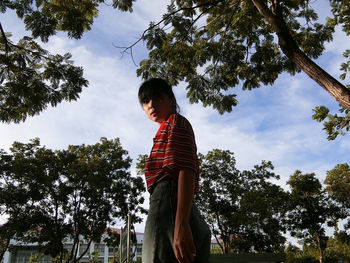 Low angle view of boy standing by trees against sky