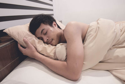 Shirtless man sleeping on bed by wall at home