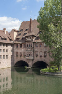 Arch bridge over river by buildings against sky