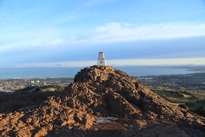 Lighthouse on cliff by sea against sky